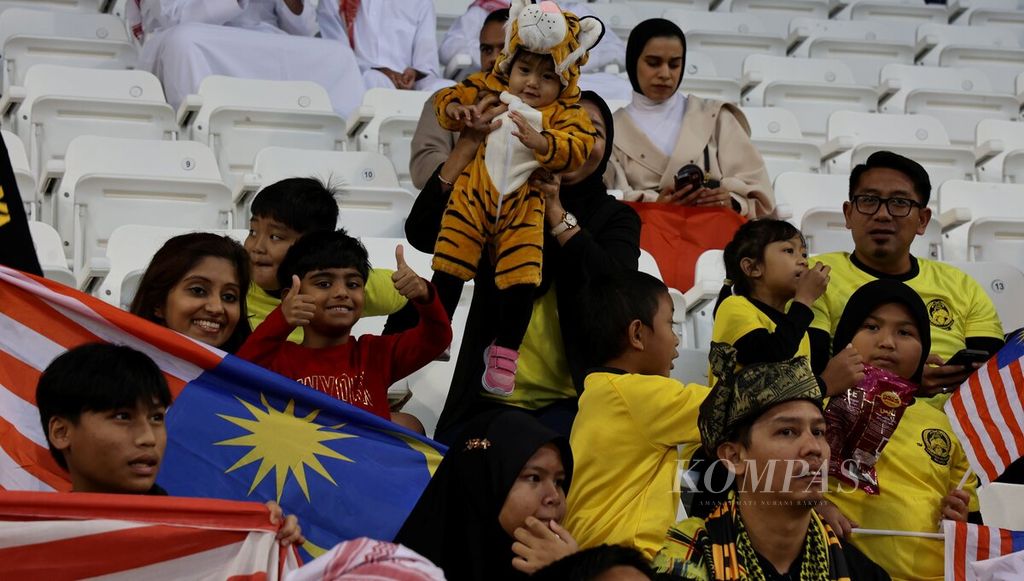 Suporter Malaysia membawa anak dengan pakaian harimau saat memberikan dukungan melawan Bahrain pada pertandingan grup E Piala Asia 2023 di Stadion Jassim bin Hamad, Qatar, Sabtu (20/1/2024). Malaysia dipastikan tersingkir setelah kalah dengan skor 0-1.