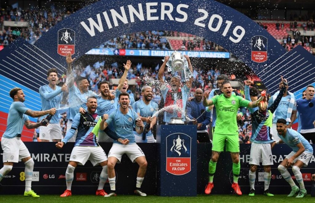 Kapten Manchester City, Vincent Kompany, mengangkat trofi kemenangan setelah mengalahkan Watford dengan skor 6-0 pada final Piala FA di Stadion Wembley, London, Sabtu (18/5/2019). Kompany kini menjadi manajer Burnley yang promosi ke Liga Primer Inggris. 
