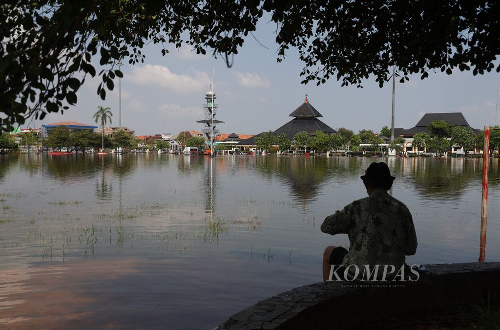 Tampak warga dengan latar banjir yang menggenangi alun-alun dan kawasan pertokoan di Kabupaten Demak, Jawa Tengah, Rabu (20/3/2024). Beberapa hari ini Kabupaten Demak dilanda banjir besar hingga menyebabkan 11 kecamatan dan 88 desa terdampak. 