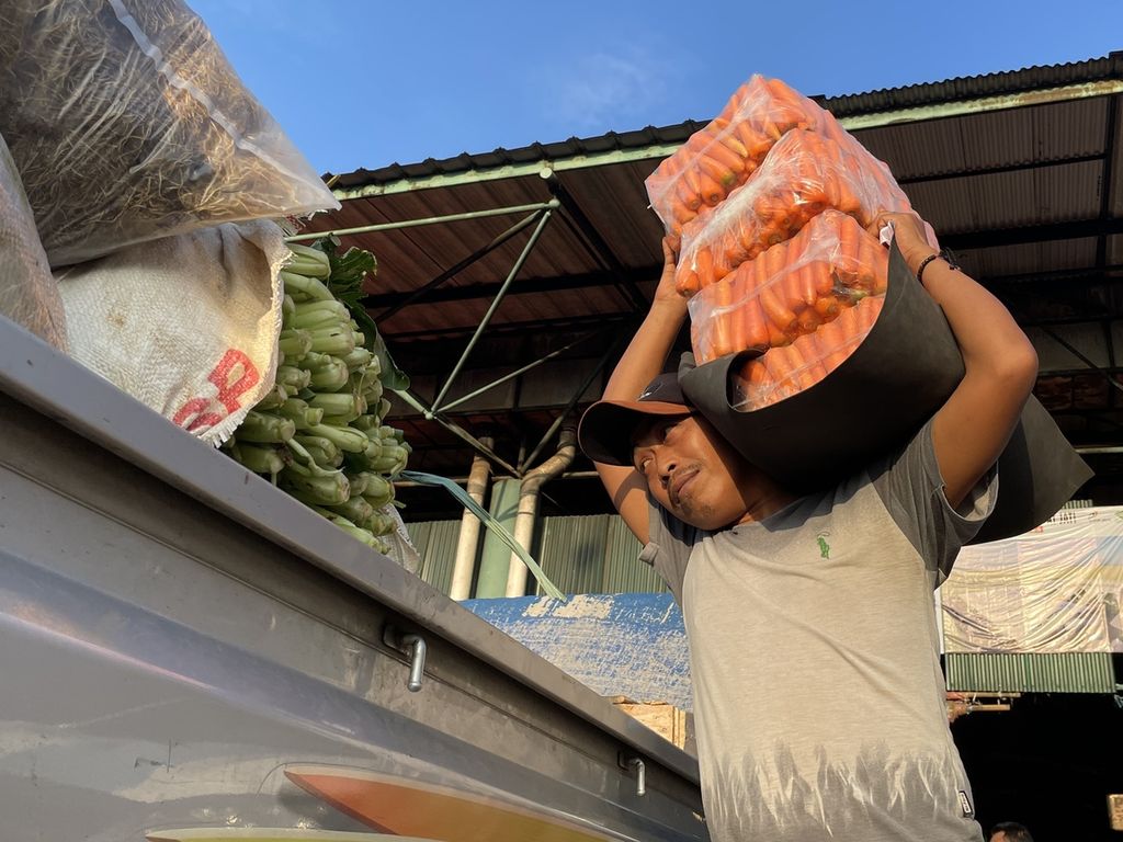 Mistori (43), kuli angkut di Pasar Induk Kramatjati, Jakarta Timur, memikul wortel dari lapak sayuran menuju pikap pembeli di area parkir, Rabu (8/3/2023).