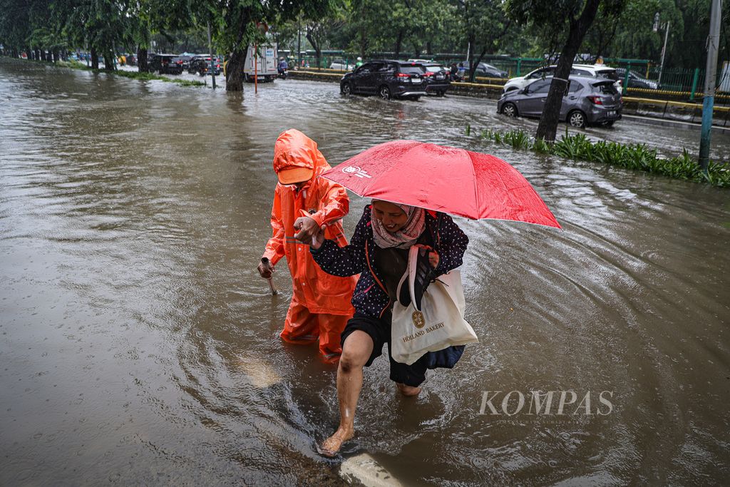 Petugas dari Dinas Lingkungan Hidup DKI Jakarta membantu warga yang menerobos genangan air di kawasan Cempaka Putih, Jakarta, Kamis (29/2/2024).