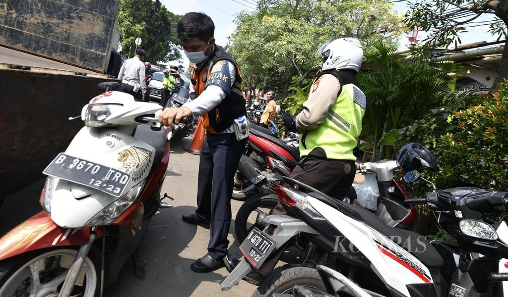 Salah seorang petugas suku dinas perhubungan memindahkan sepeda motor yang terkena razia penertiban parkir liar kendaraan di kawasan Senen, Jakarta Pusat, Rabu (2/6/2021). Dalam razia itu, puluhan sepeda motor yang diparkir di bahu jalan diangkut petugas menggunakan sejumlah truk. Meski berulang kali dilakukan penertiban, parkir liar tetap marak dan banyak dijumpai di sejumlah lokasi di Jakarta.