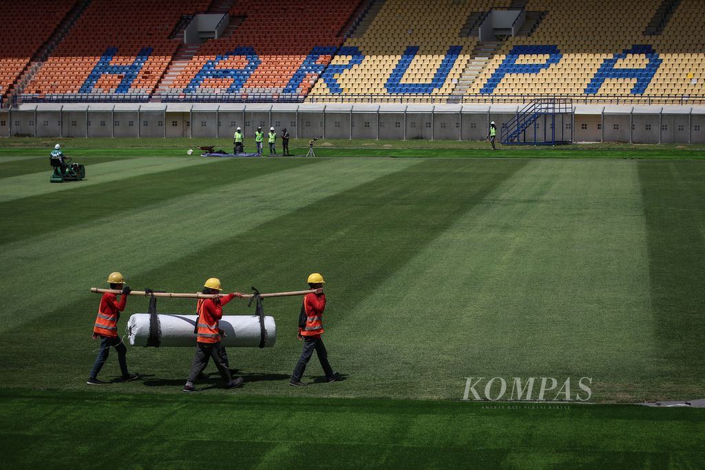 Tiga pekerja mengangkut gulungan rumput sintetis di Stadion Si Jalak Harupat, Kabupaten Bandung, Senin (3/4/2023). Si Jalak Harupat menjadi salah satu stadion yang diajukan sebagai arena Piala Dunia U-17. 