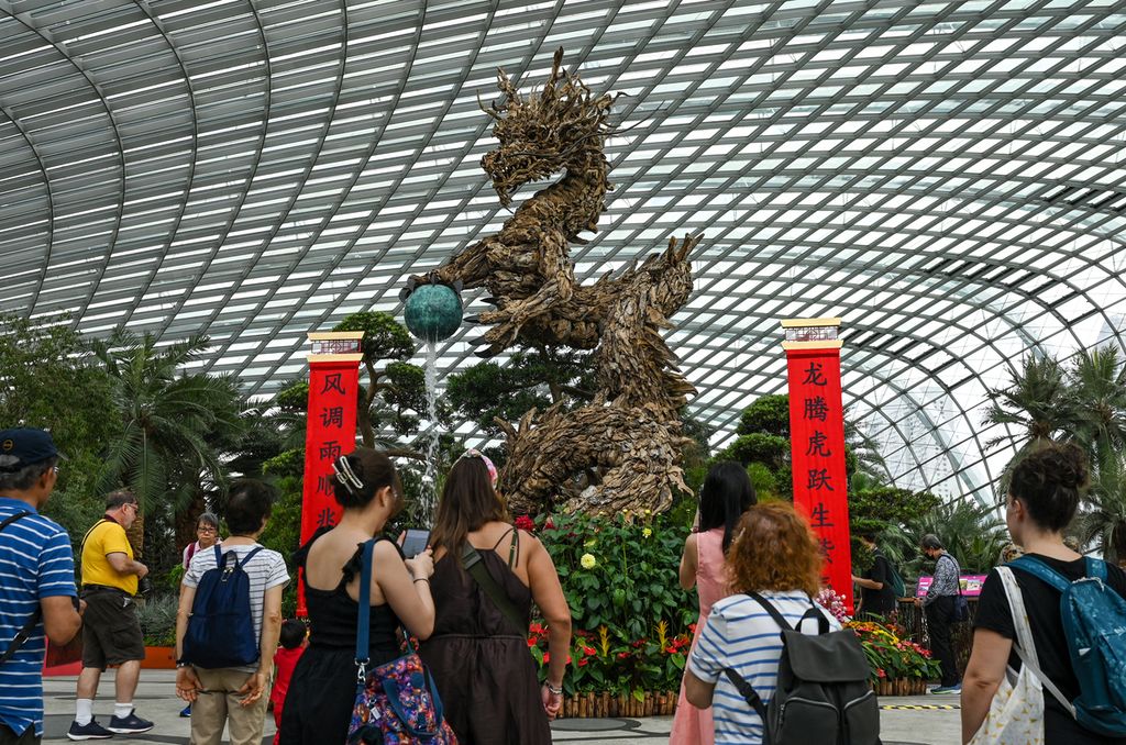 Para pengunjung memotret patung kayu bertema naga yang dipajang untuk merayakan Tahun Baru Imlek di dalam kubah bunga di Gardens by the Bay di Singapura, Kamis (1/2/2024).