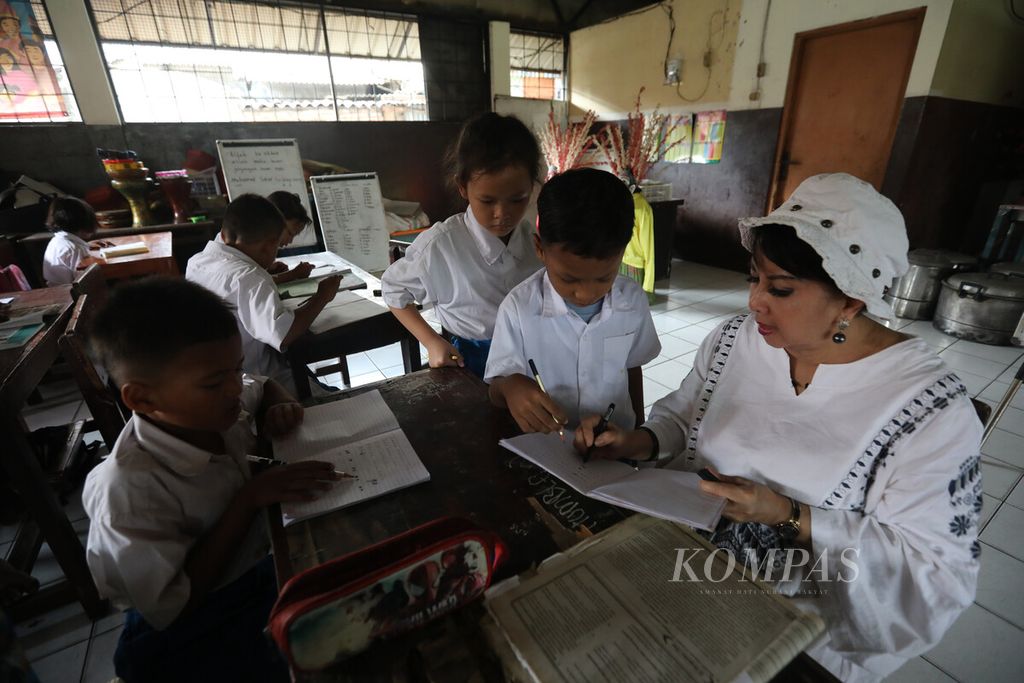 Ibu guru Rosi (kanan) memeriksa latihan soal anak didiknya di Sekolah Darurat Kartini yang diasuh ibu guru kembar Sri Irianingsih dan Sri Rossyati di ruang kelas yang menempati bangunan semipermanen di kawasan Ancol, Jakarta Utara, Jumat (5/5/2023).
