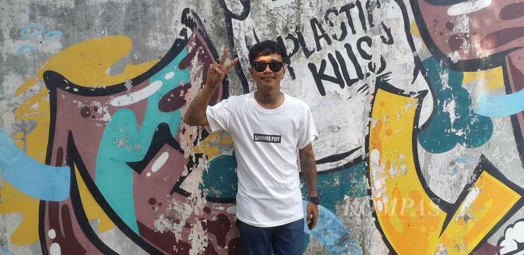 Folker Lukas Adi Wijoyo dengan latar belakang grafiti karyanya yang ia gambar di tembok sebuah rumah di kawasan Ciputat, Tangerang Selatan, Banten. Foto diambil 16 September 2023.