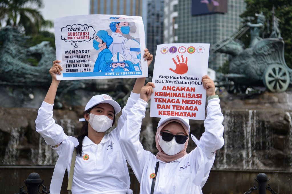 Two health workers participating in the action held up posters containing messages against the Health Bill during a demonstration in the area of the Arjuna Wiwaha Horse Statue, Central Jakarta, Monday (8/5/2023).