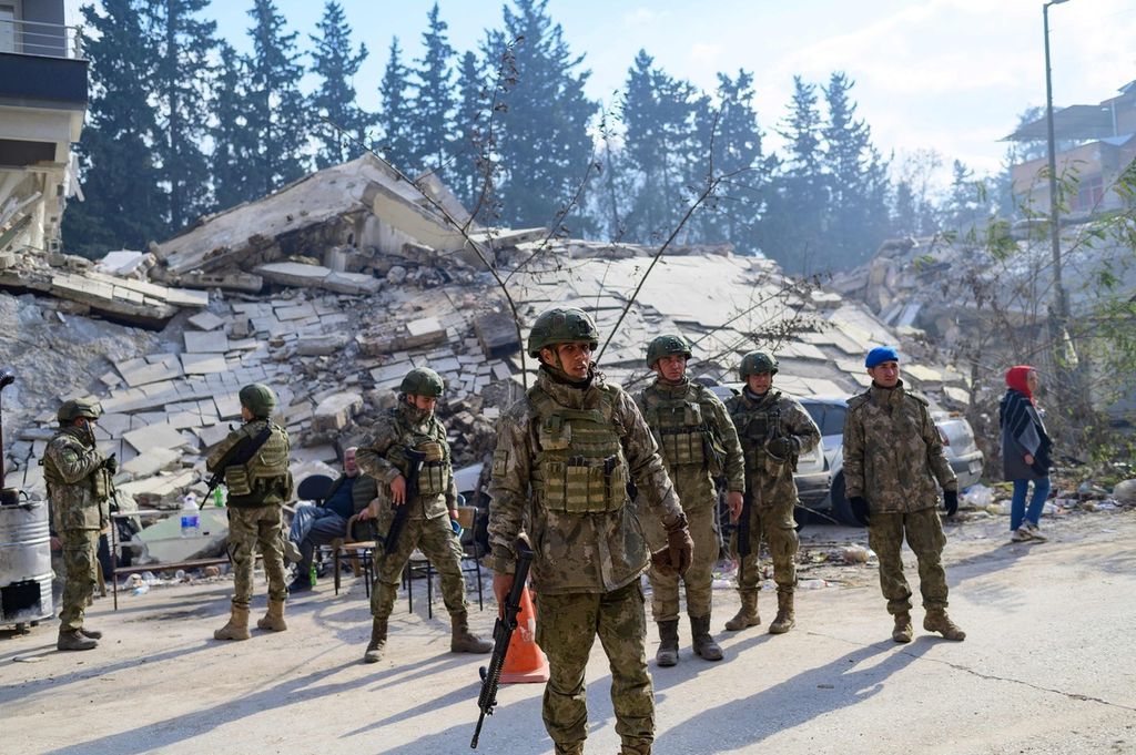 Tentara Turki berdiri di sebelah gedung yang hancur di Hatay, 11 Februari 2023, akibat gempa bermagnitudo 7,8 yang mengguncang wilayah tenggara negara itu. Sedikitnya 24.000 orang tewas akibat bencana tersebut. 