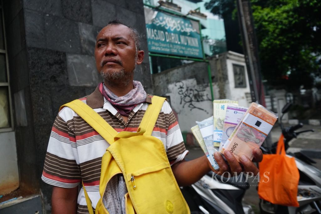 Jumahan Purba (47) menjajakan jasa penukaran pecahan uang kertas Rp 1.000 sampai Rp 10.000 di tepi jalan di daerah Kebayoran Lama, Jakarta Selatan, Selasa (18/4/2023). 