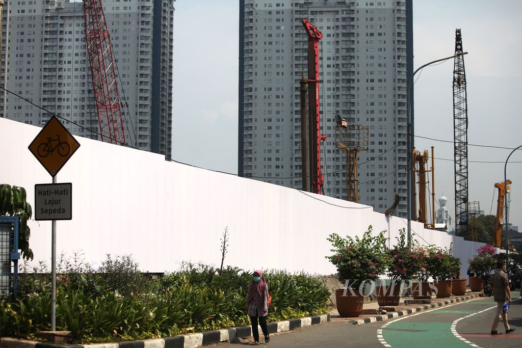 Warga melintas di sekitar proyek pembangunan gedung pencakar langit Oasis Central Sudirman di Jalan Jenderal Sudirman, Jakarta, Kamis (8/6/2023).  Gedung dengan konsep ramah lingkungan dan tahan gempa ini ditargetkan selesai pada 2029. 