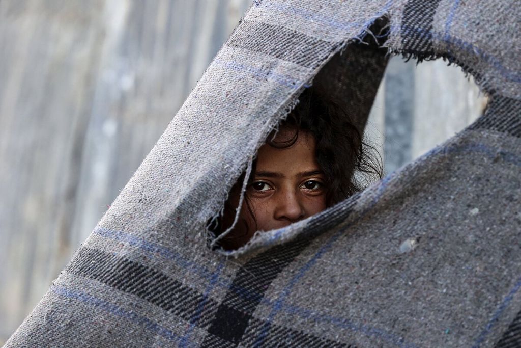 Seorang anak Palestina melihat dari balik kain saat kampanye vaksinasi Covid-19 untuk warga di Kota Gaza, Kamis (2/12/2021). 