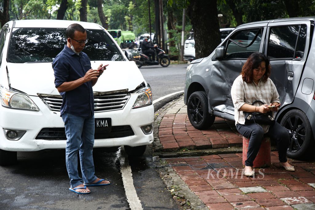 Pengemudi dua kendaraan yang terlibat kecelakaan sibuk dengan telepon seluler mereka seusai kejadian di jalan Leuser, Kebayoran Baru, Jakarta Selatan, Rabu (27/10/2021). Kecelakaan disebabkan kelalaian pengemudi mobil minibus yang bermain telepon seluler saat mengemudi. 