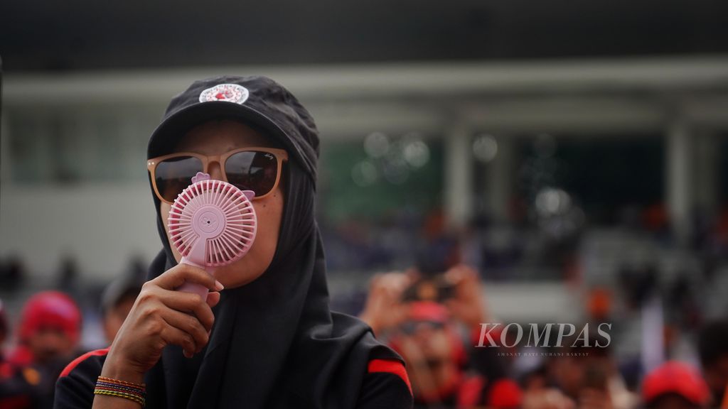 Seorang buruh yang hadir saat Mayday Fiesta 2024 di Stadion Madya Gelora Bung Karno, Jakarta, menggunakan kipas angin untuk mengusir hawa panas, Rabu (1/5/2024). 