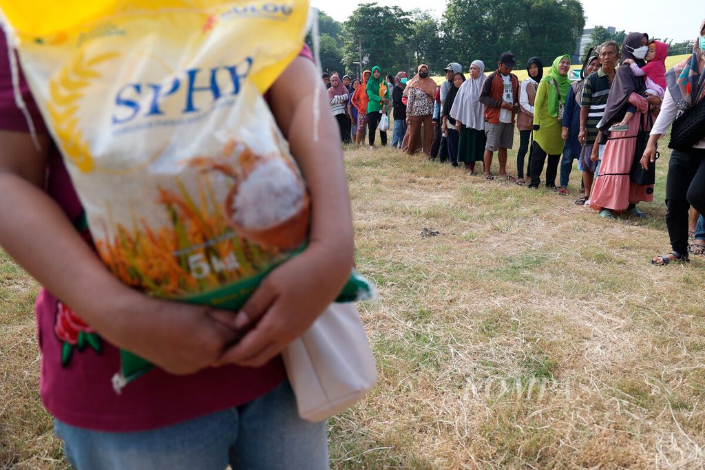 Warga membawa sekantong beras kemasan dengan latar belakang antrean saat penyelenggaraan pasar murah di Lapangan Garnisun, Kalisari, Kota Semarang, Jawa Tengah, Selasa (5/3/2024). 