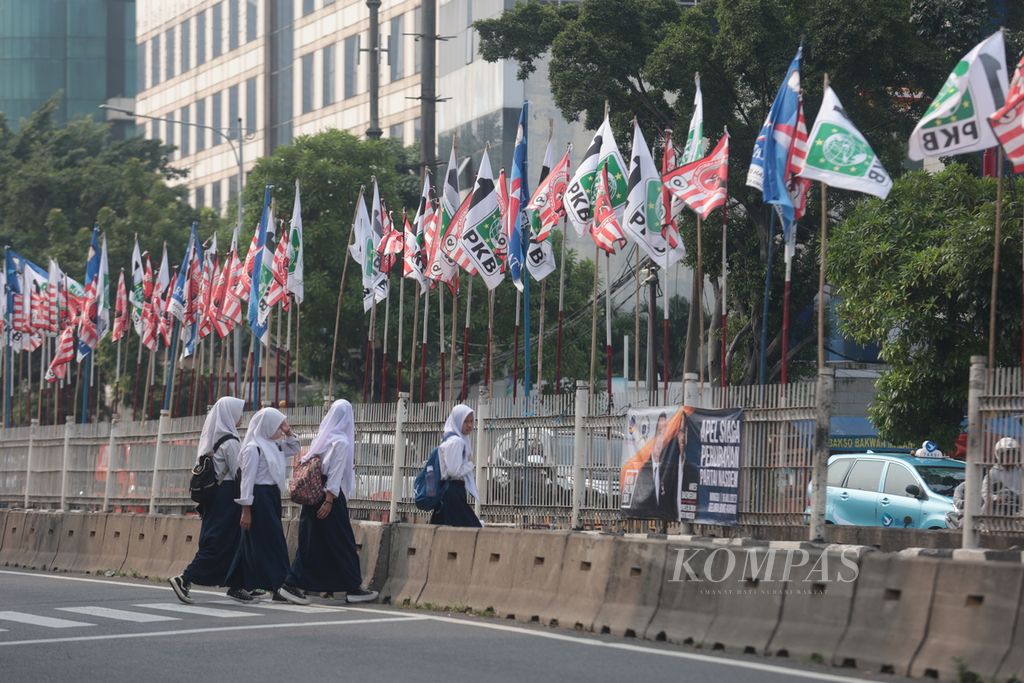 Sejumlah pelajar melintas di pagar pembatas jalan yang disesaki bendera partai politik peserta Pemilu 2024 di kawasan Mampang Prapatan, Jakarta, Kamis (13/7/2023). 