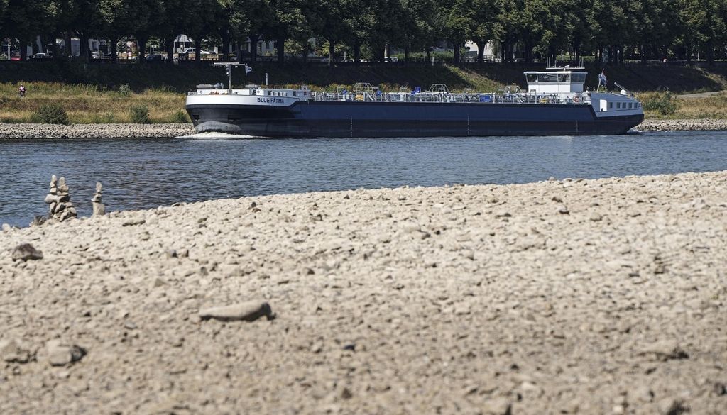 Sebuah kapal berlayar menyusuri Sungai Rhine yang tengah surut airnya di wilayah Cologne, Jerman, Rabu (10/8/2022). Ketinggian permukaan air di Sungai Rhine menurun drastis, menyebabkan kapal logistik bertonase besar kesulitan melintasi sungai ini. 