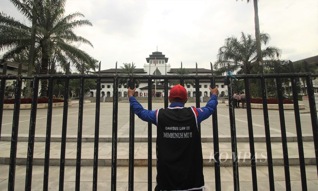 A protesting worker is seen holding onto the fence of the Gedung Sate building in Bandung City, West Java on Thursday (11/25/2021). The workers are rejecting the Job Creation Law and demanding a 10 percent increase in the minimum wage for districts/cities in West Java in 2022.