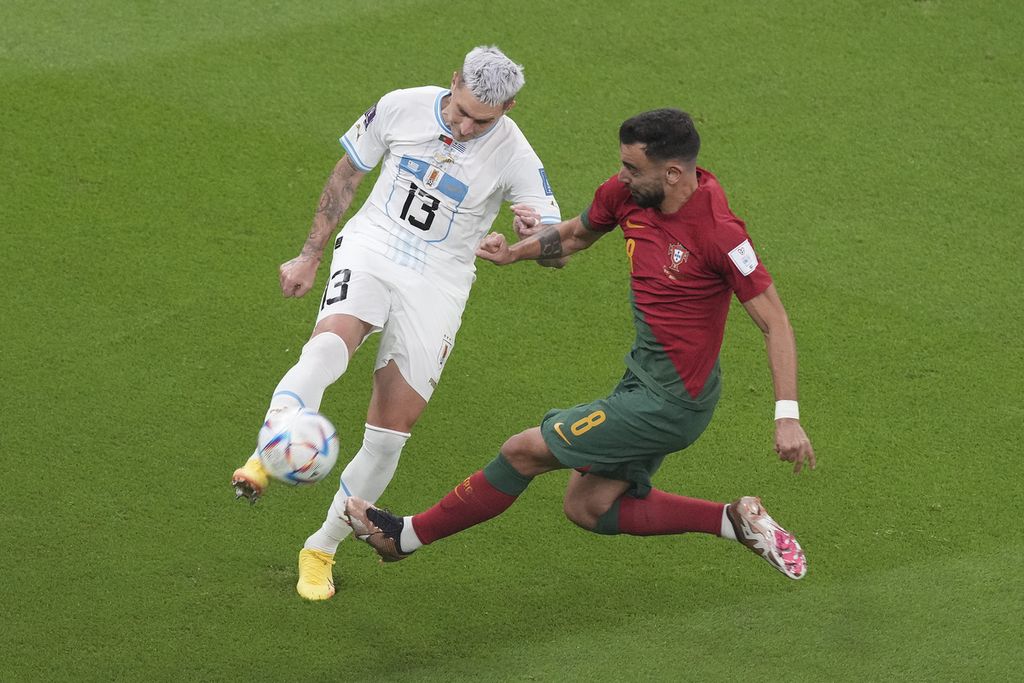 Pemain Portugal, Bruno Fernandes (kanan), berebut bola dengan pemain Uruguay, Guilermo Varela, saat bertanding di fase Grup H Piala Dunia Qatar di Stadion Iconic, Lusail, Selasa (29/11/2022) dini hari WIB.