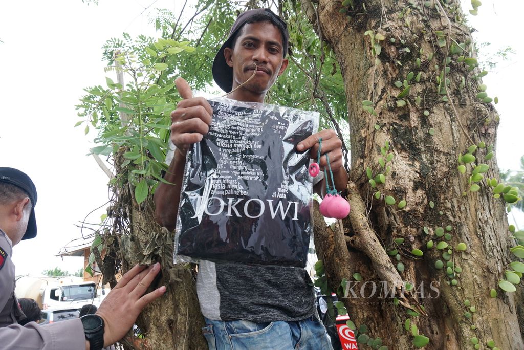 Seorang warga memamerkan kaus dari Presiden Joko Widodo yang ia tangkap setelah dilemparkan oleh Pasukan Pengamanan Presiden, Kamis (19/1/2023), di depan Bendungan Kuwil-Kawangkoan, Kecamatan Kalawat, Minahasa Utara, Sulawesi Utara.
