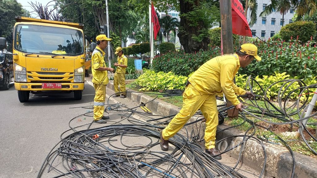 Petugas Dinas Bina Marga DKI Jakarta, Rabu (11/1/2023) memotong kabel udara dan menurunkan kabel-kabel yang sudah terpotong di Jalan Kebon Sirih, Jakarta Pusat. 