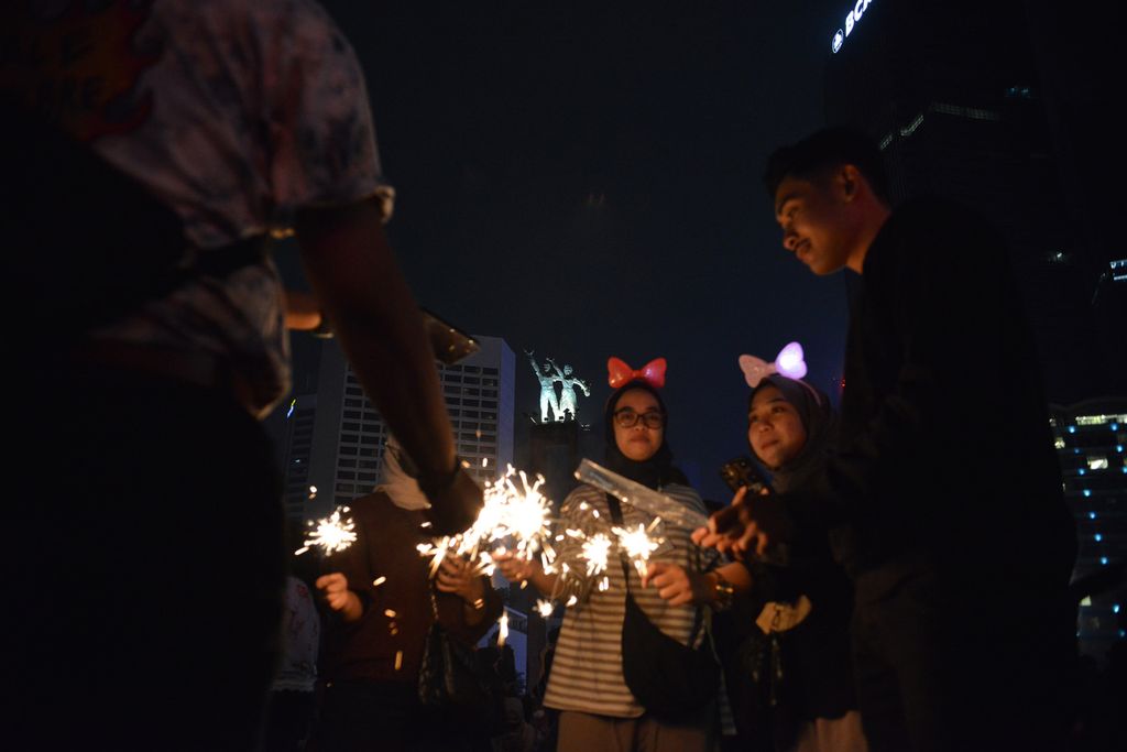 Sejumlah warga bermain kembang api di depan Patung Selamat Datang di Bundaran Hotel Indonesia (HI), Jakarta Pusat, Minggu (1/1/2023). Bundaran HI menjadi salah satu kawasan yang dipilih warga untuk merayakan pergantian tahun.