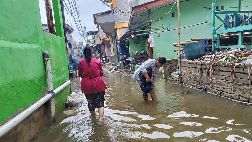 Warga berjalan melintasi genangan air setinggi 20 sentimeter akibat hujan yang mengguyur sedari malam hingga siang di Kampung Nelayan Muara Angke, Kelurahan Pluit, Kecamatan Penjaringan, Jakarta Utara, Rabu (1/2/2023). 