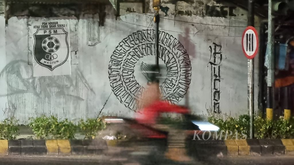 Pengendara motor melintas di depan tembok yang terpasang mural logo PSM Madiun di kawasan Kejuron, Kota Madiun, Jawa Timur, Kamis (20/7/2023). 