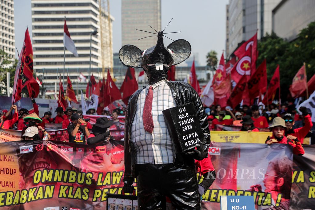 Demonstran membawa poster dan spanduk di belakang patung tikus raksasa di Jalan MH Thamrin, Jakarta, Kamis (10/8/2023). Ribuan peserta aksi yang terdiri dari organisasi-organisasi buruh melakukan aksi di Jalan MH Thamrin.  