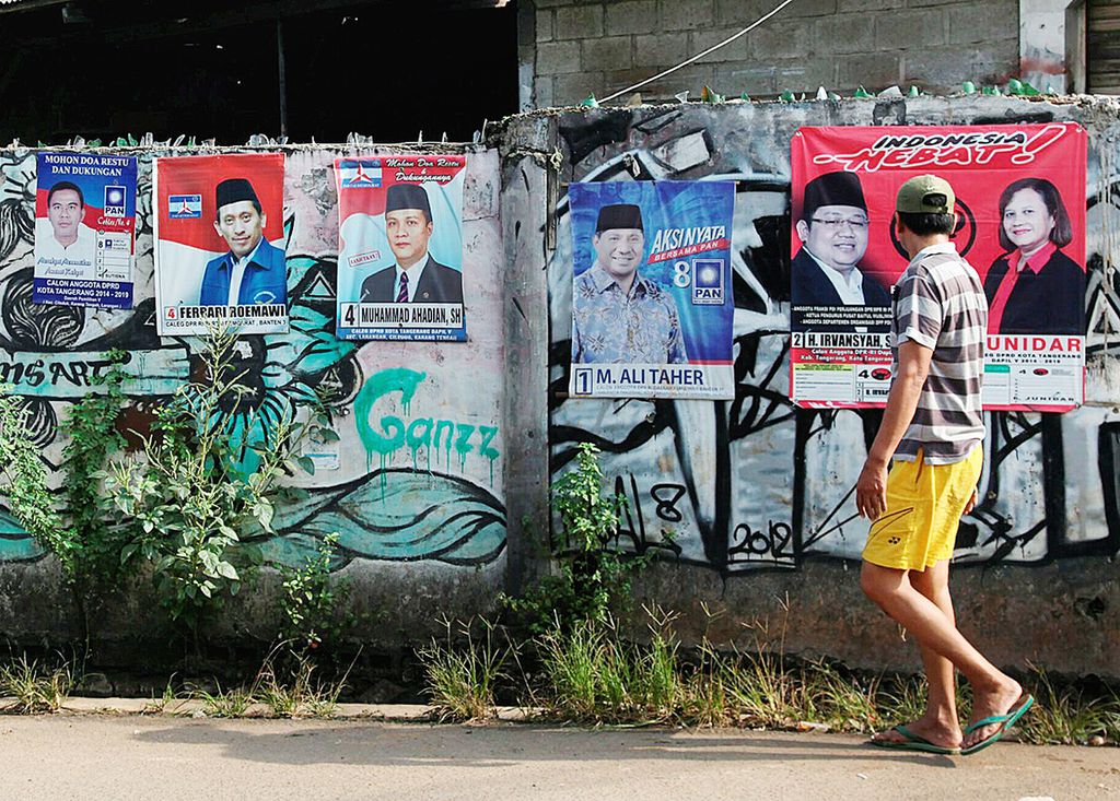 Warga melintas di depan poster caleg yang masih terpasang di salah satu sudut Kota Tangerang, Banten, Minggu (27/4/2014). Keberadaan poster caleg seusai pencoblosan itu hanya menambah poster sampah politik di sudut-sudut kota. 