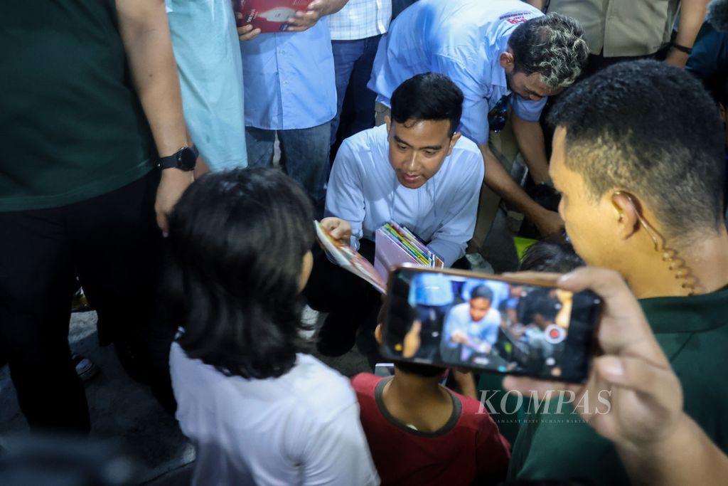 Calon wakil presiden nomor urut 2, Gibran Rakabuming Raka, membagikan buku kepada anak-anak di Jalan Rawa Bebek 1, Penjaringan, Jakarta Utara, Jumat (1/12/2023). 