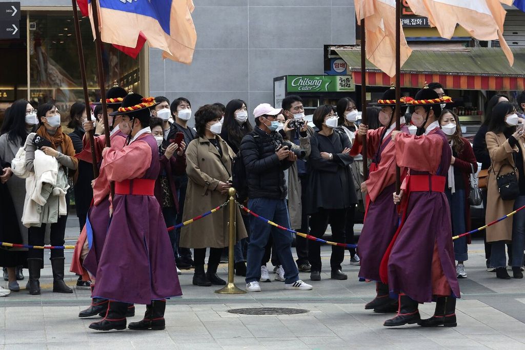 Warga yang mengenakan masker menyaksikan upacara pergantian pengawal kerajaan di dekat pintu gerbang Istana Deoksu di Seoul, Korea Selatan, Jumat (13/11/2020). 