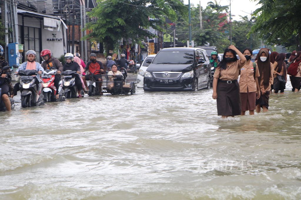 Pengendara dan pejalan kaki mencoba menerobos banjir di Jalan Dr Mansyur, Kota Medan, Sumatera Utara, Sabtu (19/11/2022). Hujan lebat pada Jumat malam membuat sejumlah permukiman dan ruas jalan di Kota Medan tergenang banjir.
