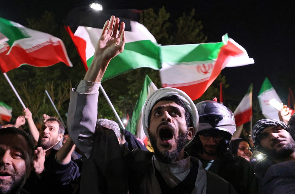 Demonstran mengibarkan bendera Iran dan bendera Palestina saat berkumpul di depan Kedutaan Besar Inggris di Teheran, 14 April 2024, setelah Iran melancarkan serangan <i>drone</i> dan rudal ke Israel. Pengawal Revolusi Iran mengonfirmasi pada hari itu bahwa serangan tersebut dilakukan terhadap Israel sebagai pembalasan atas serangan pesawat tanpa awak yang mematikan pada 1 April di konsulatnya di Damaskus. 