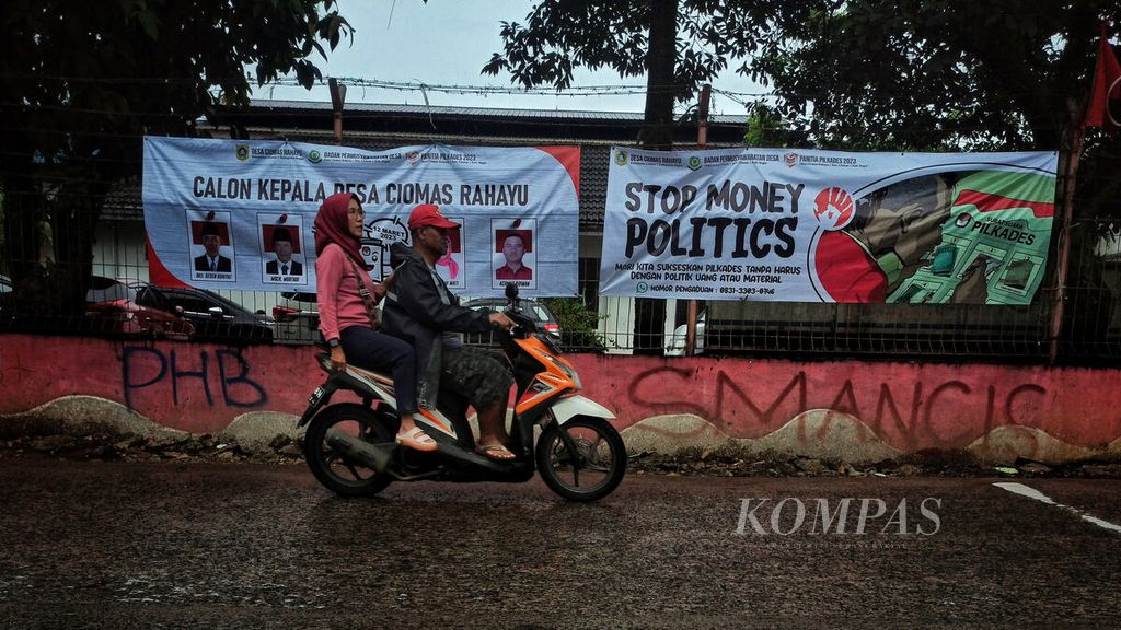 Warga melintasi spanduk berisi seruan antipolitik uang terpasang di salah satu tepi Jalan Raya Ciomas, Bogor, Jawa Barat, Minggu (12/2/2023). 