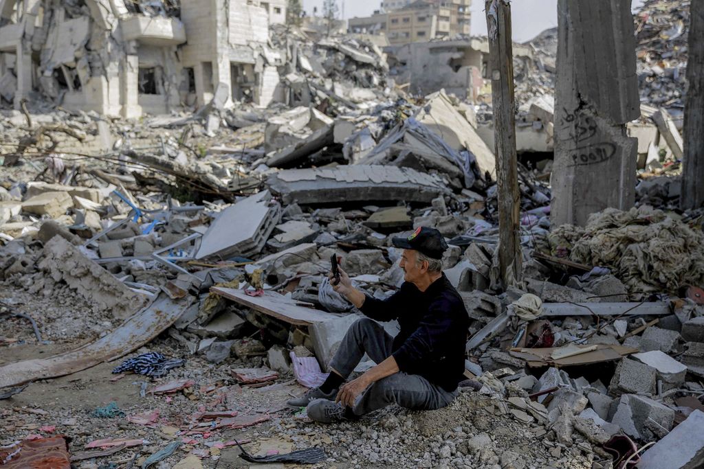 Seorang warga Palestina menggunakan ponselnya saat duduk di tengah reruntuhan bangunan yang hancur di Kota Gaza saat jeda pertempuran empat hari yang mulai berlaku pada 24 November 2023. 