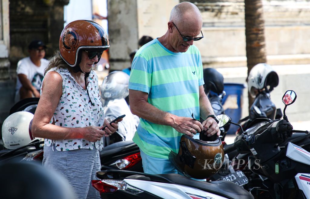 Turis asing mengenakan helm sebelum mengendarai sepeda motor sewaan di pantai Kuta, Bali, Sabtu (18/3/2023). Sepeda motor sewaan menjadi pilihan oleh sebagian turis asing sebagai transportasi selama wisata di Bali karena berbagai alasan seperti berbiaya murah dan praktis.