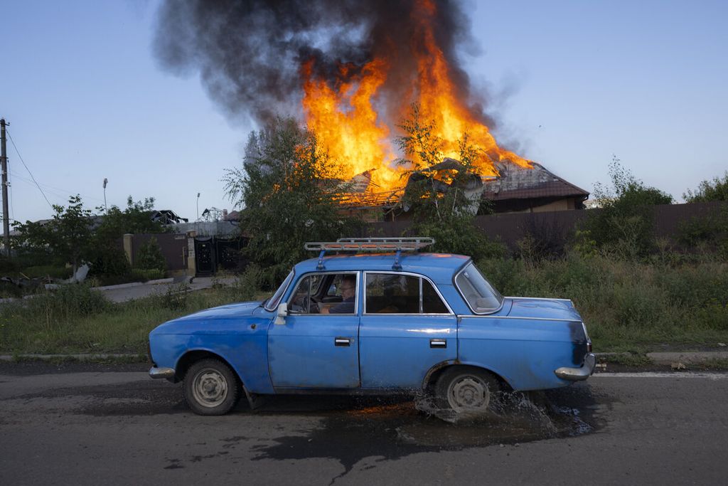 Warga mengendarai mobil melintasi sebuah rumah yang terbakar setelah terjadi serangan dari Rusia di Bakhmut, Ukraina, Rabu (27/7/2022). 