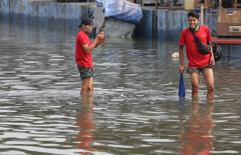 Warga berfoto di tengah genangan banjir rob yang menggenangi kompleks Pelabuhan Perikanan Samudera Nizam Zachman, Muara Baru, Penjaringan, Jakarta Utara, Jumat (5/6/2020). 