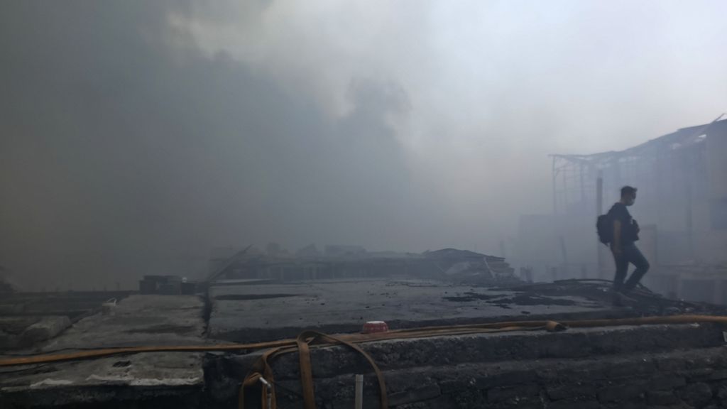 Seorang warga membawa barang dan melintas di antara puing dan asap pekat hitam menyelimuti permukiman warga di RW 003, Jalan Kapuk Utara 2, Kapuk Muara, Penjaringan, Jakarta Utara, ludes terbakar, Minggu (30/7/2023) sore.