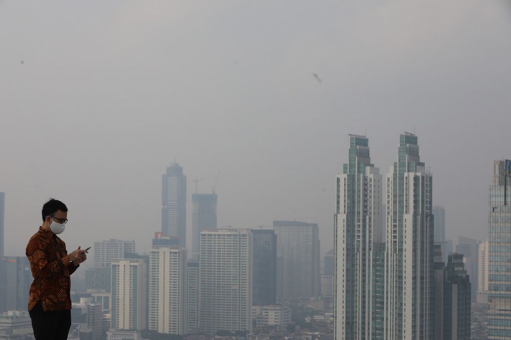 Pekerja kantoran menggunakan ponselnya dengan latar belakang kabut yang menyelimuti sebagian besar wilayah Jakarta pada Selasa (9/6/2020) pagi. 