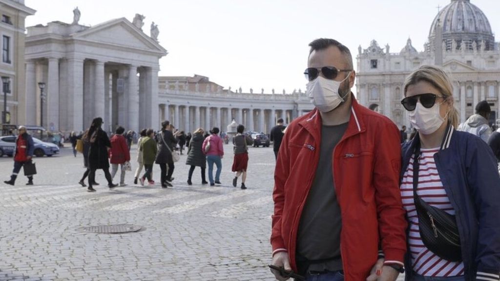 Sepasang pengunjung yang berada di luar St Peter Square, Vatikan, Roma, Italia, menggunakan masker untuk melindungi diri, Kamis (27/2/2020). Italia telah menjadi sumber penularan wabah Covid-19 di Eropa.