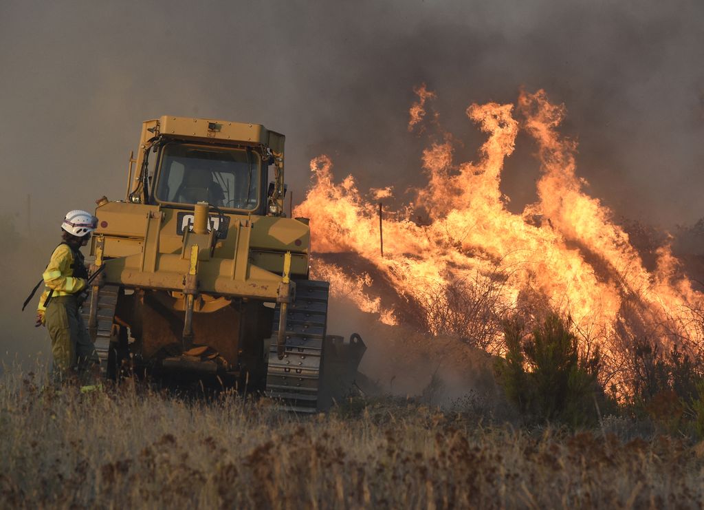Petugas pemadam kebakaran menggunakan buldoser saat mereka memadamkan api di Desa Tabara, dekat Zamora, barat laut Spanyol, Senin (18/7/2022). Ratusan warga desa terdampak dievakuasi untuk menghindari korban jiwa.