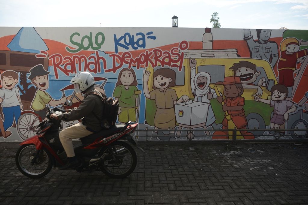 Pekerja melintas di depan mural tentang pilkada sebelum merakit kotak suara di gudang Komisi Pemilihan Umum (KPU) Kota Surakarta, Jawa Tengah, Rabu (18/11/2020). 