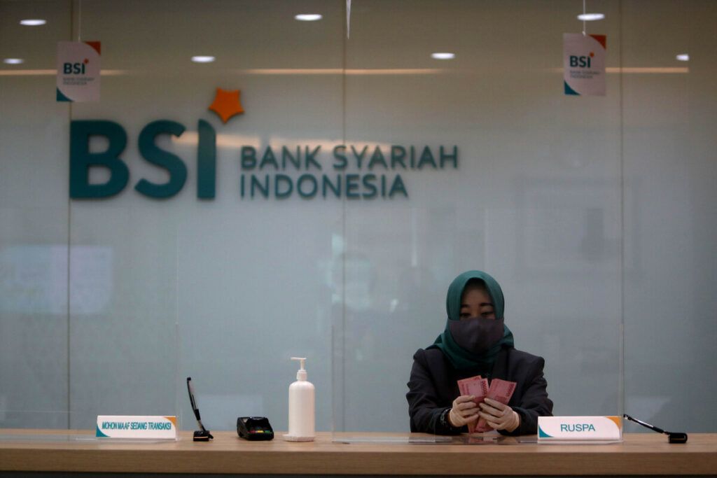 Teller Bank Syariah Indonesia menghitung uang rupiah di Kantor Cabang Hasanudin, Blok M, Jakarta, Senin (1/2/2021). Bank yang merupakan hasil merger dari PT Bank BRI Syariah Tbk, PT Bank BNI Syariah, dan PT Bank Syariah Mandiri tersebut, resmi beroperasi pada Senin (1/2/2021). Bank beraset Rp 240 triliun ini diharapkan dapat memberikan efek domino bagi ekonomi syariah dan rantai pasok industri halal dalam negeri. BSI saat ini berada di posisi ke-7 dalam daftar sepuluh besar bank terbesar di Indonesia dari sisi aset.