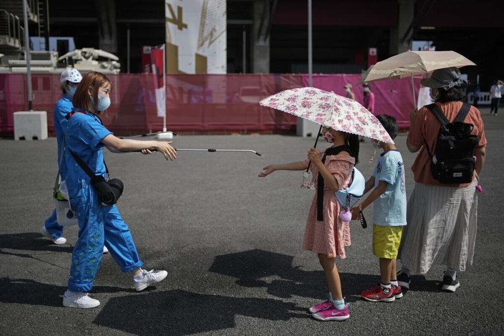 Petugas menyemprotkan alkohol ke tangan seorang anak di Oyama, Jepang, pada tangga 25 Juli 2021 sebagai protokol kesehatan selama pandemi Covid-19.