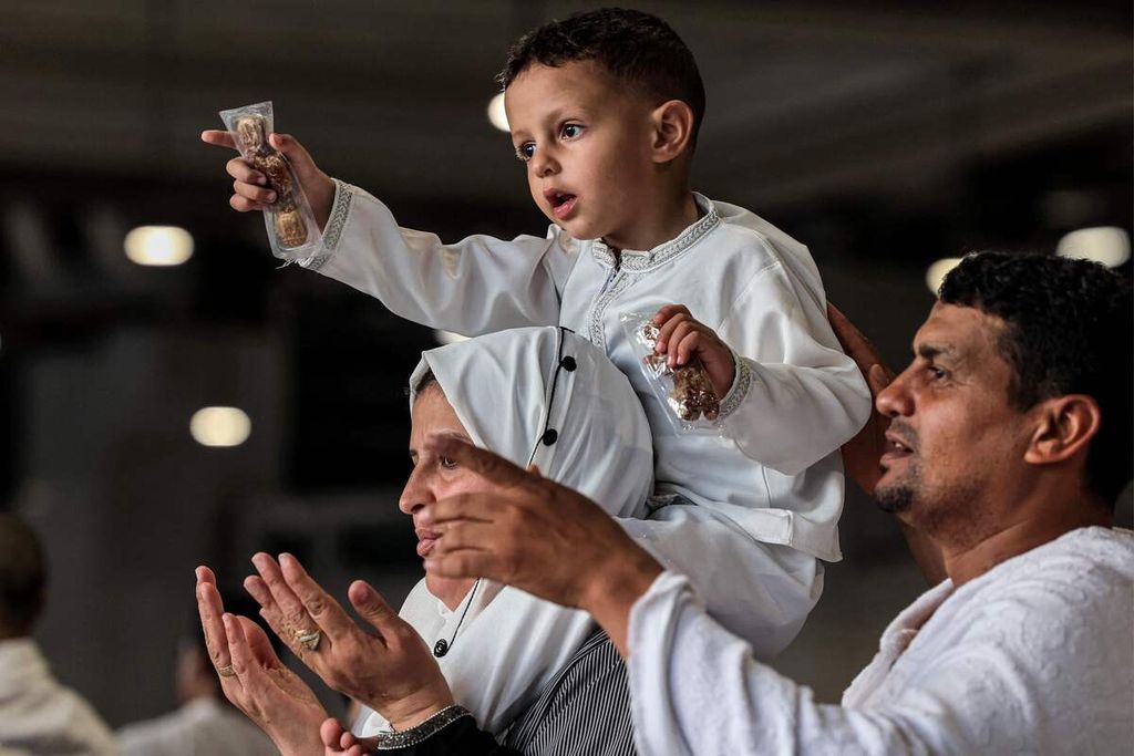 Seorang anak laki-laki dengan bungkusan kurma duduk di atas bahu seorang jemaah wanita yang salat di Masjidil Haram, di kota suci umat Islam Mekkah pada hari Jumat terakhir bulan suci Ramadhan, Jumat (5/4/2024). Sebagian besar negara di Arab sudah menetapkan Idul Fitri pada Rabu (10/4/2024).