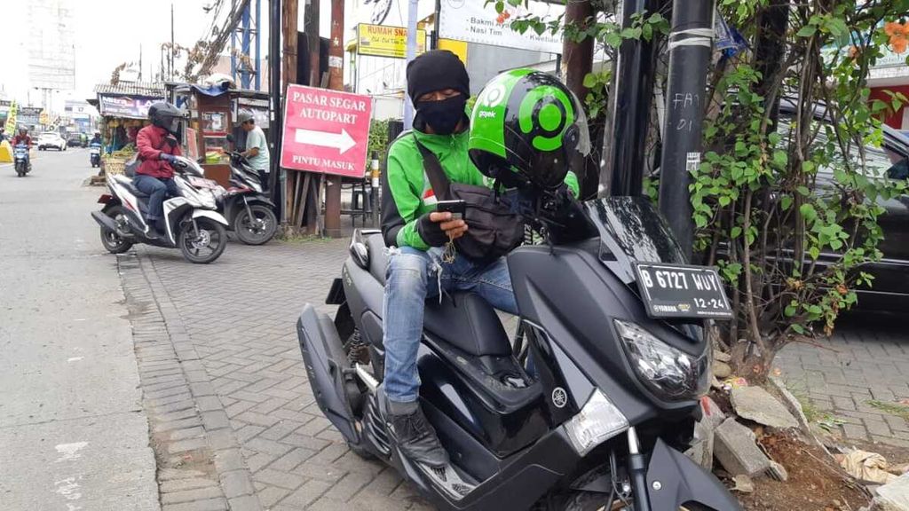 Faisal, pengemudi ojek daring, menunggu pesanan masuk ke aplikasi ponselnya di Jalan Cinere Raya, Depok, Jabar, Kamis (9/7/2020).