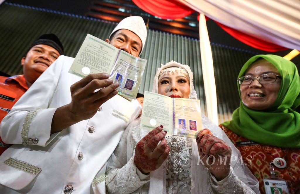 Pasangan pengantin menunjukkan buku nikah seusai ijab kabul dalam acara nikah massal pada malam pergantian tahun di Balai Kota DKI Jakarta, Selasa (31/12/2019).