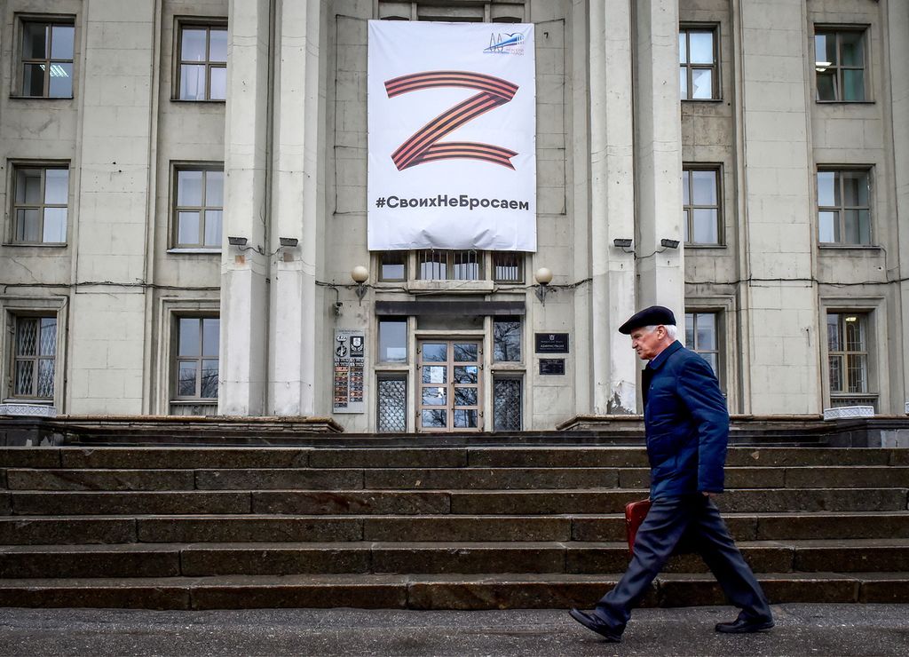 Seorang pria melintas di depan gedung yang dipasangi simbol Z dan slogan yang semuanya merupakan dukungan terhadap militer Rusia, di Saint Petersburg, Rusia, Jumat (8/4/2022).  
