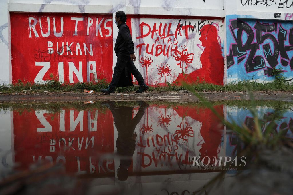 Warga melintas di depan mural berisi seruan untuk mendorong pengesahan Rancangan Undang-Undang Tindak Pidana Kekerasan Seksual yang dibuat di tembok Stadion Kridosono, Yogyakarta, Senin (10/1/2021). 